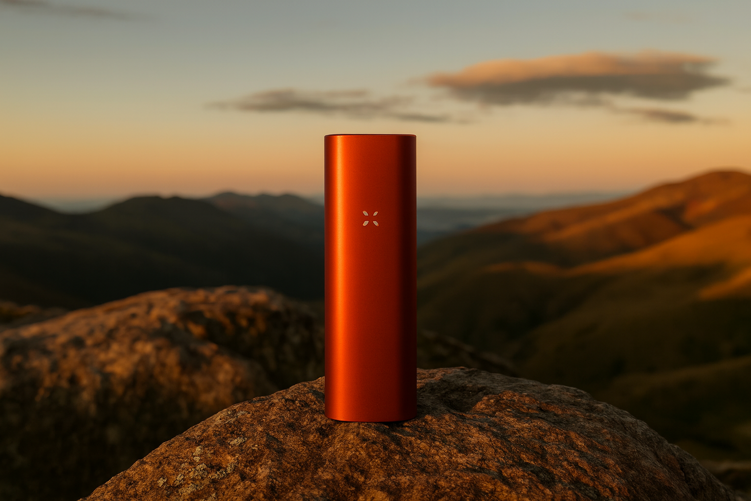 Burnt-orange PAX Mini vaporizer standing on a rugged mountain rock with golden sunset light and rolling hills in the background